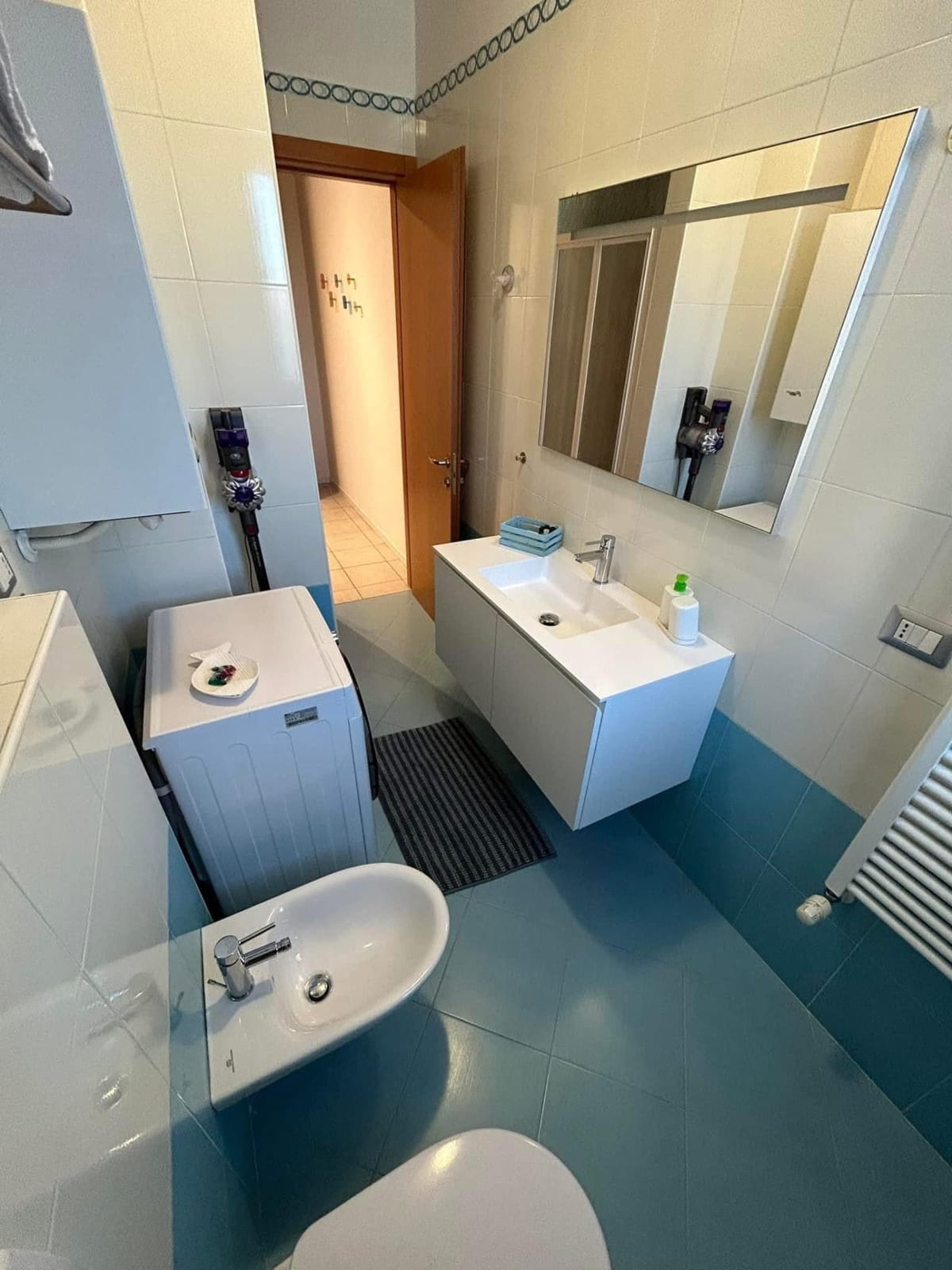 Bagno con pavimento turchese, lavabo sospeso e grande specchio