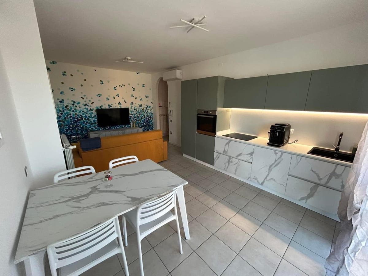 Open space con tavolo effetto marmo, cucina verde salvia e murale a pois blu sullo sfondo